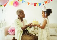 Grandmother and granddaughter holding cake at birthday party — Stock Photo