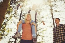 Mother carrying daughter on shoulders hiking in sunny woods — Stock Photo