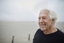 Lächelnder älterer Mann schaut am Strand weg — Stockfoto