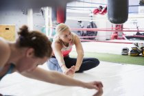Mujeres jóvenes estirando las piernas junto al ring de boxeo en el gimnasio - foto de stock