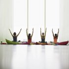 Mujeres en cojines con brazos levantados en estudio de gimnasio de yoga restaurativo - foto de stock