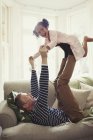 Playful multi-ethnic father balancing daughter on legs overhead on sofa — Stock Photo