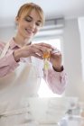 Smiling woman baking, cracking egg over bowl in kitchen — Stock Photo