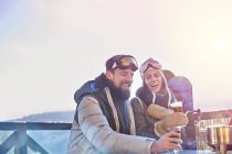 Snowboarder couple laughing, drinking cocktails on sunny balcony apres-ski — Stock Photo