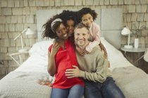 Portrait enthusiastic pregnant young family hugging on bed — Stock Photo