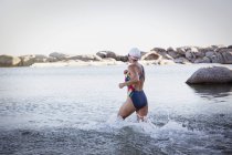 Nuotatrice d'acqua aperta femminile che corre e schizza nel surf oceanico — Foto stock