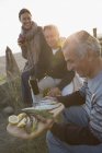 Mature friends drinking wine and barbecuing fish on sunset beach — Stock Photo