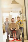 Portrait smiling children pushing father on toy car in foyer corridor — Stock Photo
