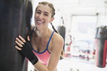 Портрет усміхнений, впевнена молода жінка-боксерка в мішку для удару в спортзалі — стокове фото