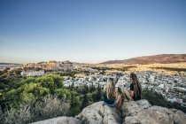 Пара, сидячи на скелі, звідки відкривається вид на ландшафт, Афіни, Греція — стокове фото