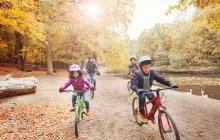 Giovane famiglia in bicicletta lungo laghetto nel parco autunnale — Foto stock