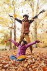 Juguetona madre e hija lanzando hojas de otoño en el parque - foto de stock