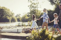 Семья держится за руки и ходит по солнечному причалу у озера — стоковое фото