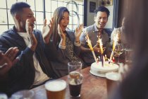 Friends cheering for woman celebrating birthday with fireworks cake at table in bar — Stock Photo