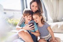 Мати і діти використовують мобільний телефон у сонячній вітальні — стокове фото