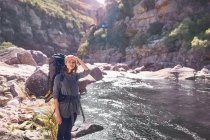 Giovane donna con zaino trekking al ruscello soleggiato remoto — Foto stock