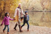 Grandmother holding hands with grandchildren walking along pond in autumn park — Stock Photo