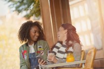 Laughing young women friends with cell phone at urban sidewalk cafe — Stock Photo