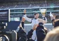 Equipo de carreras de Fórmula 1 rociando champán al piloto con trofeo, celebrando la victoria en pista deportiva - foto de stock
