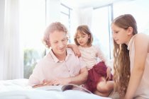Padre e figlie leggere libro sul letto — Foto stock