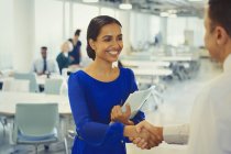 Усміхнена бізнес-леді тремтить руками з бізнесменом в офісі — стокове фото