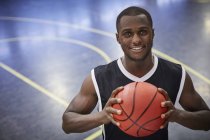 Retrato sonriente joven jugador de baloncesto masculino sosteniendo baloncesto en la cancha - foto de stock