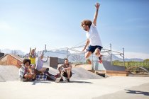 Friends watching and cheering man jumping in roller skates at sunny skate park — Stock Photo