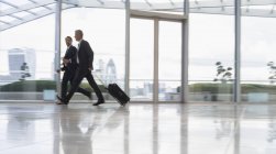Empresários andando e puxando mala no aeroporto — Fotografia de Stock
