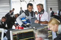 Manager and formula one driver with digital tablet talking in repair garage — Stock Photo