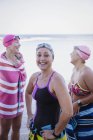 Sonrientes nadadoras femeninas con toallas al aire libre en el océano - foto de stock