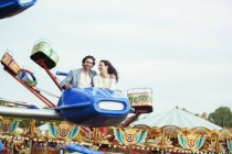 Couple enjoying ride on carousel in amusement park — Stock Photo