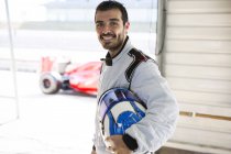 Porträt selbstbewusster männlicher Formel-1-Rennfahrer mit Helm in Reparaturwerkstatt — Stockfoto