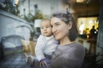 Lächelnde Mutter hält kleine Tochter am Fenster — Stockfoto