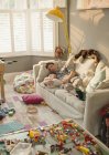 Виснажений батько і дитина син спить на дивані в безладному вітальні з іграшками — стокове фото