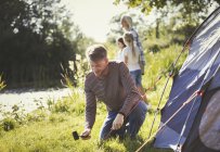 Father pitching tent at sunny lakeside campsite — Stock Photo