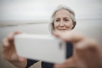 Femme âgée prenant selfie avec téléphone caméra sur la plage d'hiver — Photo de stock