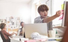 Серьёзные женщины-дизайнеры рассматривают клейкие заметки на компьютере в офисе — стоковое фото