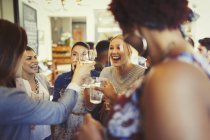 Enthusiastic women friends toasting wine glasses at bar — Stock Photo