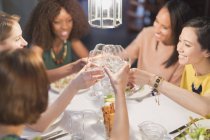 Mujeres sonrientes amigas brindando por copas de vino blanco cenando en la mesa del restaurante - foto de stock