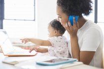 Mother working from home with daughter sitting on her lap — Stock Photo