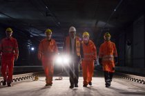 Male foreman and construction workers walking in dark construction site underground — Stock Photo