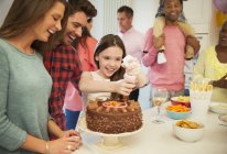 Smiling family icing chocolate cake in kitchen — Stock Photo