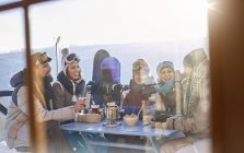 Snowboarder friends drinking and eating at balcony table apres-ski — Stock Photo