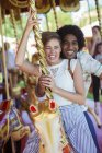 Jovem casal multirracial sorrindo no carrossel no parque de diversões — Fotografia de Stock