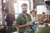 Retrato confiado joven diseñador masculino beber café en el taller - foto de stock