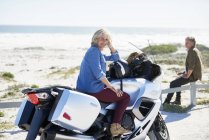 Портрет впевнена старша жінка на мотоциклі на сонячному пляжі — стокове фото