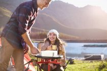 Young couple camping, cooking at camping stove at sunny lakeside — Stock Photo