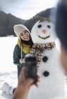 Man photographing woman with snowman — Stock Photo