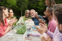 Affectueux multi-ethnique couple de personnes âgées câlins célébration anniversaire à la table de patio — Photo de stock