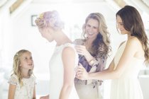 Сестра невесты и подружка невесты помогают невесте переодеться в домашнюю комнату — стоковое фото
